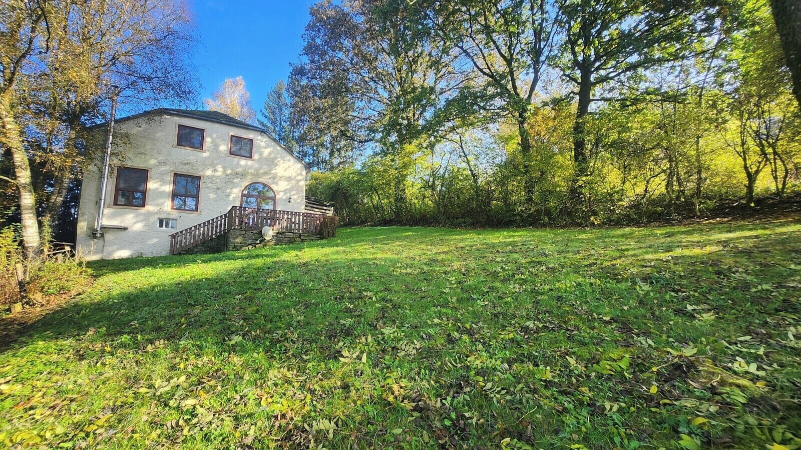 A two-story house with a stone facade, a wooden deck, and a grassy yard.