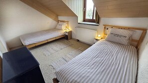 Habitació petita i acollidora amb dos llits individuals, un radiador, una finestra i un escriptori.
