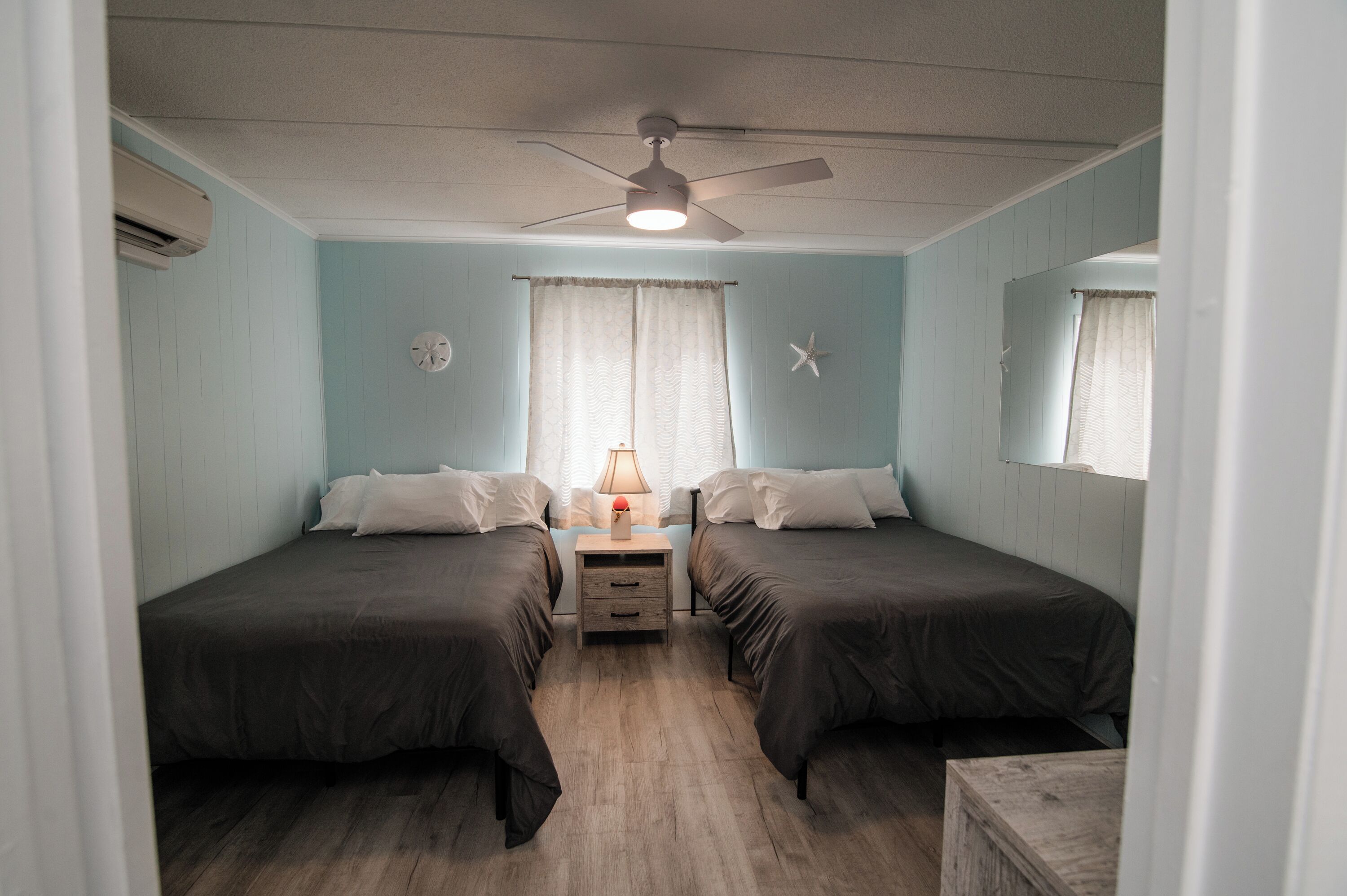 Un dormitorio con dos camas, ventilador de techo, mesita de noche y una decoración con forma de estrella de mar.