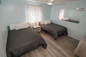 Una habitación con dos camas, una mesita de noche, una lámpara, un espejo y un ventilador de techo.