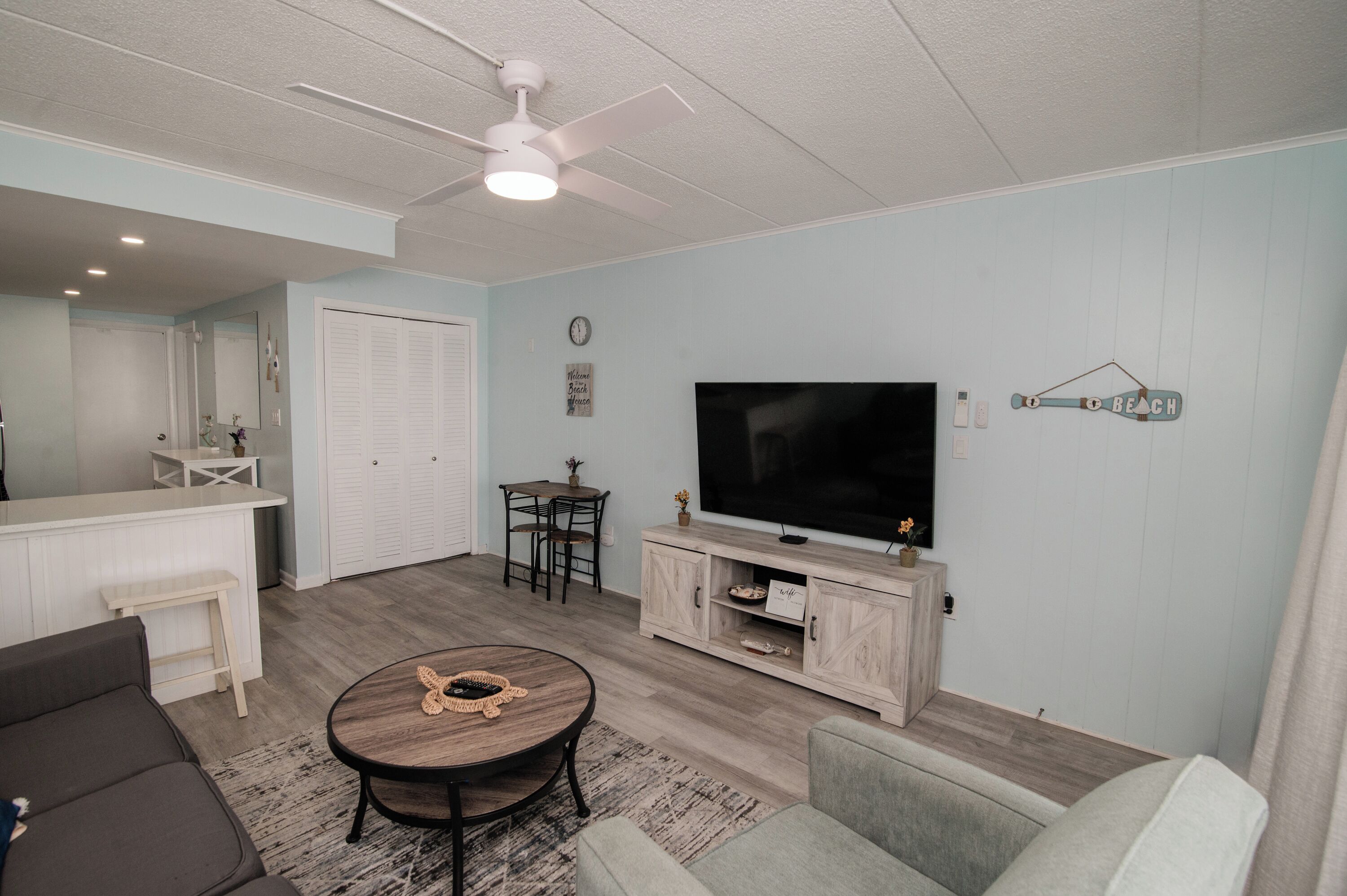 A living room with a flat-screen TV, a ceiling fan, a coffee table, and a sofa.