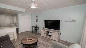 A living room with a flat-screen TV, a ceiling fan, a coffee table, and a sofa.