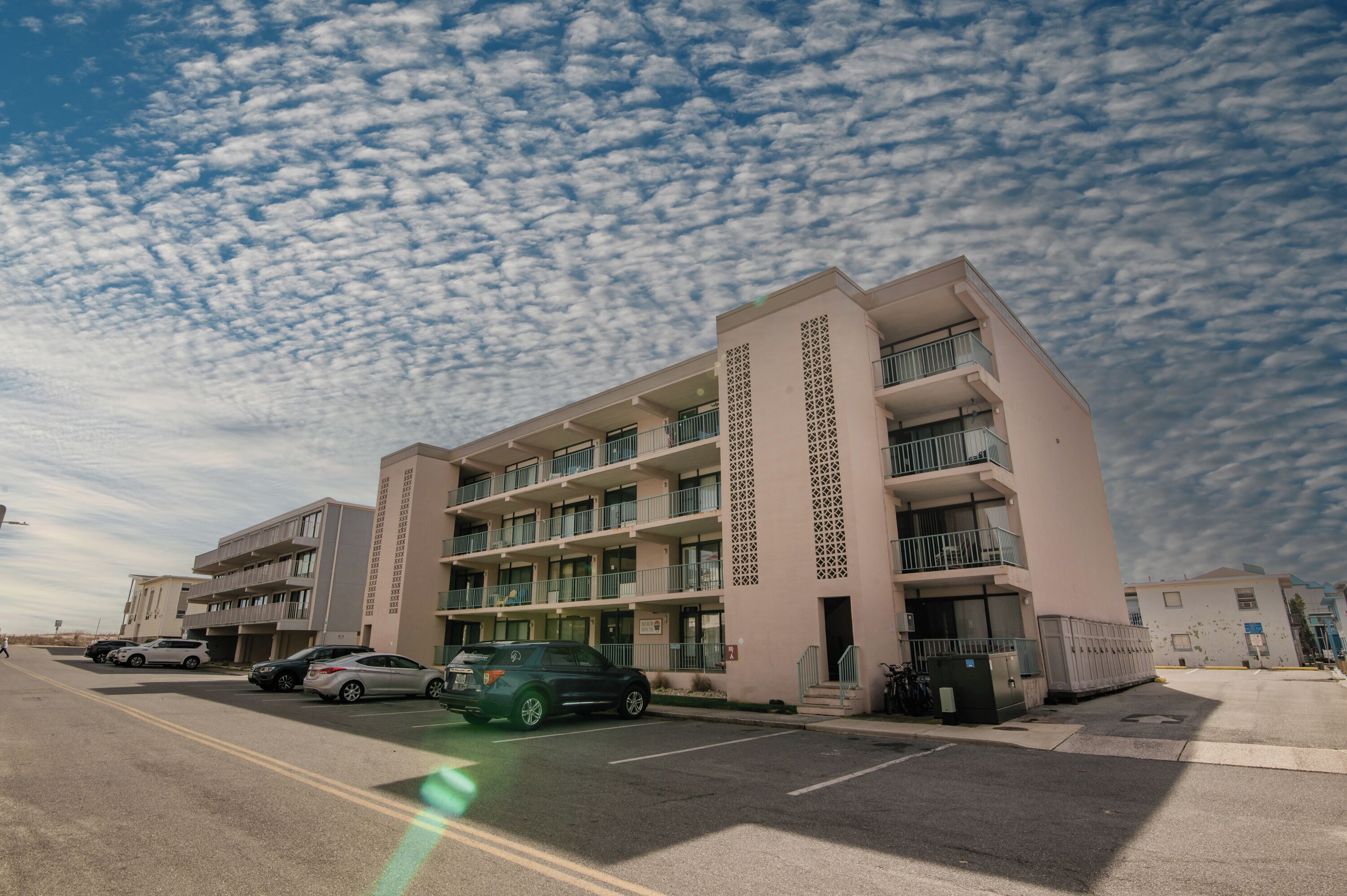 Un hotel de varios pisos con balcones, un estacionamiento y un cielo despejado.