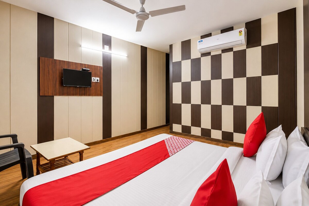A hotel room with a bed, a desk, a chair, a television, and an air conditioning unit.