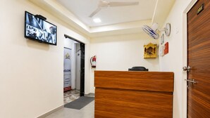 A hotel reception area with a wooden desk, a television mounted on the wall, and a door labeled '101'. - Hotel New Suryam (Ahmedabad)