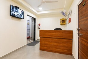 A hotel reception area with a wooden desk, a television mounted on the wall, and a door labeled '101'. - Hotel New Suryam (Ahmedabad)