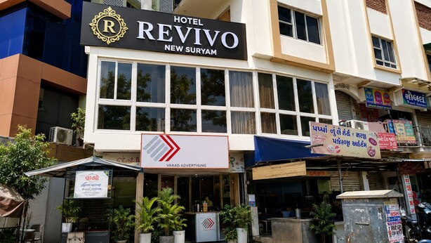 A hotel named 'Hotel Revivo' with a prominent sign, located in a commercial area with various shops and advertisements. - Hotel New Suryam (Ahmedabad)