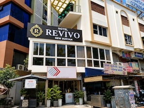 Un hotel llamado 'Hotel Revivo' con un letrero llamativo, situado en una zona comercial con diversas tiendas y anuncios.