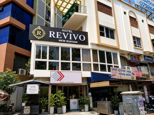 A hotel named 'Hotel Revivo' with a prominent sign, located in a commercial area with various shops and advertisements. - Hotel New Suryam (Ahmedabad)
