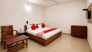A hotel room with a bed, a wooden chair, a small table, a wardrobe, and a ceiling fan. - Hotel New Suryam (Ahmedabad)