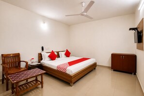 A hotel room with a bed, a wooden chair, a small table, a wardrobe, and a ceiling fan. - Hotel New Suryam (Ahmedabad)