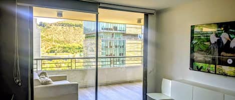 A bedroom with a sliding glass door leading to a balcony, a bed, a white sofa, and a mounted TV.