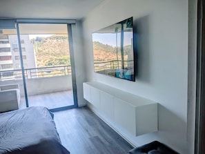 A modern bedroom with a bed, a TV mounted on the wall, and a balcony with a view of a hillside. - Spectacular Golf Course: Newly Remodeled Apartment + Free Parking (Las Condes)