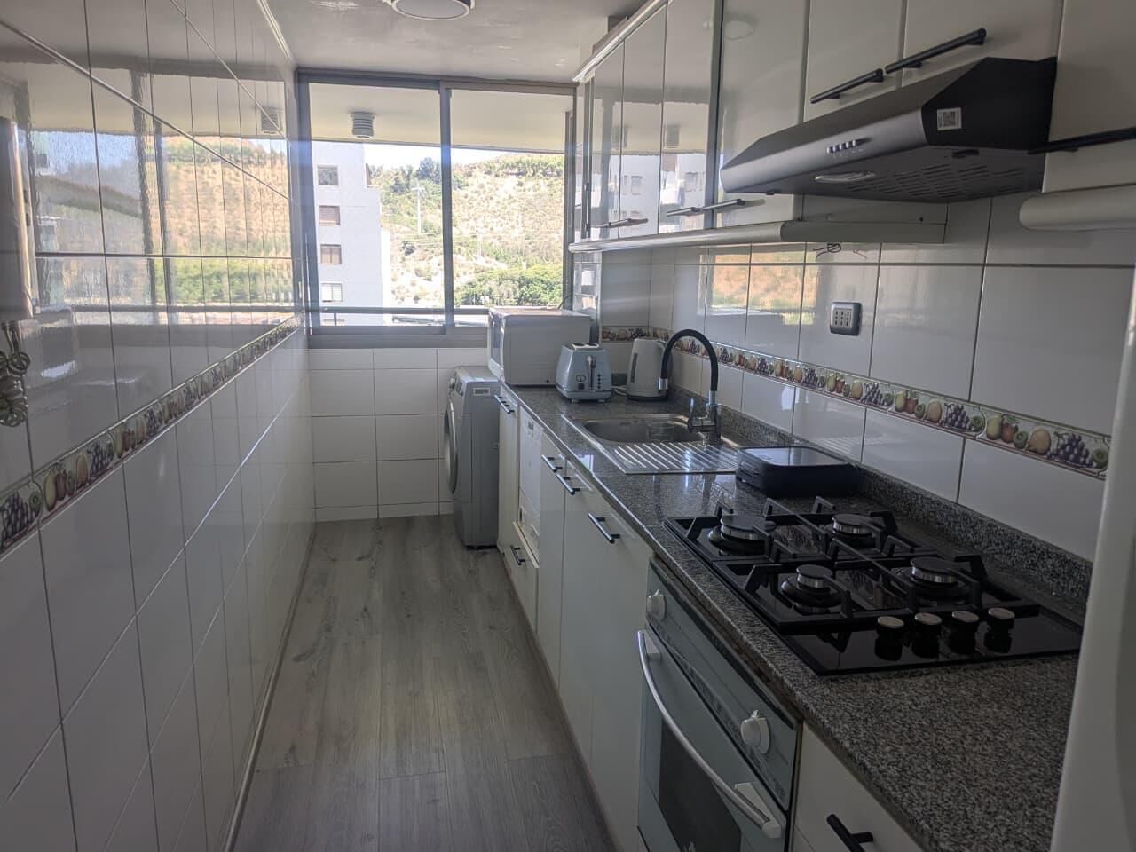 Una cocina con alacenas blancas, estufa a gas y ventana con vistas al exterior.