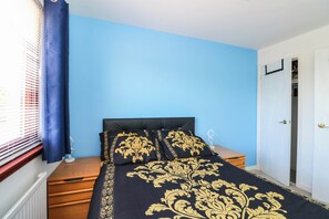 Un dormitorio con cama, mesita de noche, ventana con persianas y puerta.