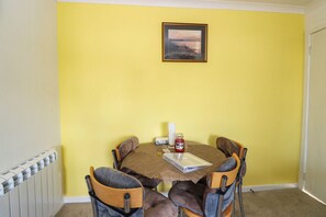 Un comedor con una pared amarilla, un cuadro enmarcado y una mesa con sillas.