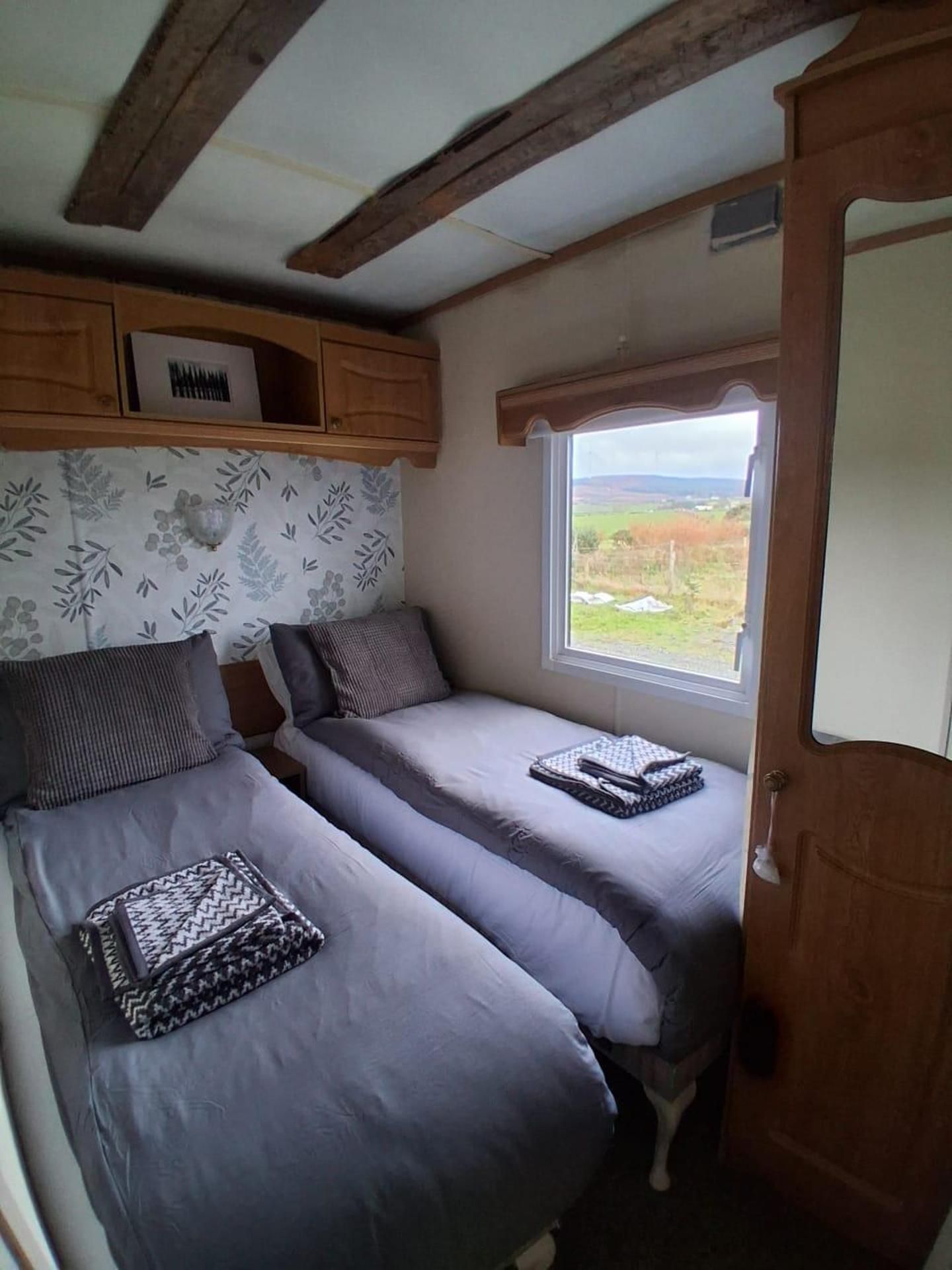 A compact room with two beds, a window with a view, and a wooden ceiling.