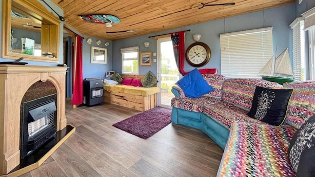 Ein gemütliches Blockhaus-Interieur mit Holzbalkendecke, Kamin, einer Couch und einem Essbereich.