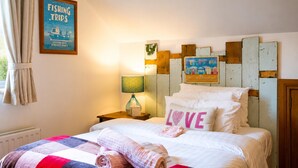 Ein Hotelzimmer mit Bett, Nachttisch, Lampe, einer Wand mit dem Schild 'Fishing Trips' und einem Schild 'Beach Huts'.