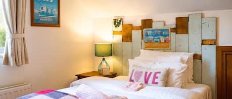 A hotel room with a bed, a nightstand, a lamp, a wall with a 'Fishing Trips' sign, and a 'Beach Huts' sign.