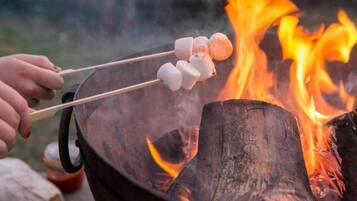 A hand holding a stick with marshmallows over a fire.