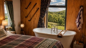 A bedroom with a large bed, a bathtub, and a window with a view of greenery. - Cottage Sleeps 4 With Parking and Sea Views (Lecamy)