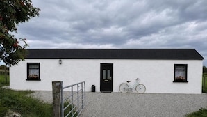 A white building with a black door and windows, a gravel driveway, and a bicycle parked in front. - Cottage Sleeps 4 With Parking and Sea Views (Lecamy)