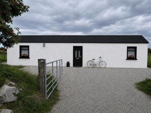 Ein weißes Gebäude mit schwarzem Eingang und Fenstern, einer Schotterauffahrt und einem Fahrrad davor.