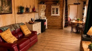 A cozy living room with a red leather sofa, wooden walls, and a dining area with a table and chairs. - Cottage Sleeps 4 With Parking and Sea Views (Lecamy)