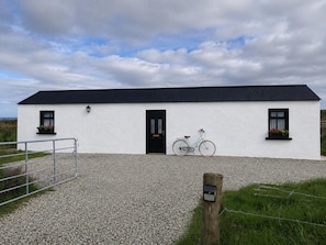 A white building with a black roof, a black door, and two windows with flower boxes. - Seaside Retreat Cottage in Carrowmenagh (Lecamy)