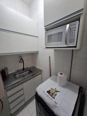 Cocina compacta con un lavamanos de acero inoxidable, un microondas y un rollo de papel higiénico sobre una mesita.
