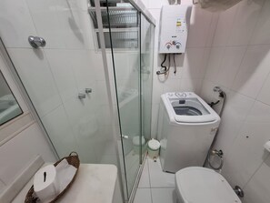 Un baño pequeño con ducha de mampara, inodoro y lavadora.