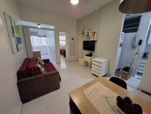 Una sala de estar con un sofá, una televisión, un escritorio y una mesa de comedor.