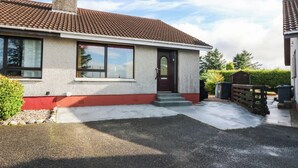 A two-story house with a red and white exterior, a chimney, and a front door with a small porch. - 7 Creag Ruadh (Isle of Lewis)