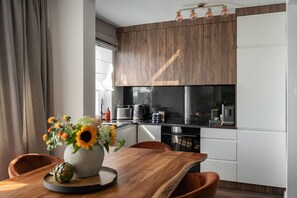 Una cocina moderna con armarios de madera, encimera negra y zona de comedor con mesa y sillas de madera.