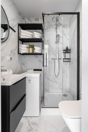 A modern bathroom with a glass-enclosed shower, a white toilet, a black vanity with a mirror, and a small white appliance. - Secret Garden by Lion Apartments Gdańsk (Gdańsk)