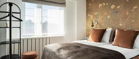 A bedroom with a bed, a window with a view, a radiator, and a wall with floral wallpaper.