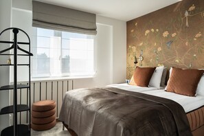 A bedroom with a bed, a window with a view, a radiator, and a wall with floral wallpaper. - Secret Garden by Lion Apartments Gdańsk (Gdańsk)