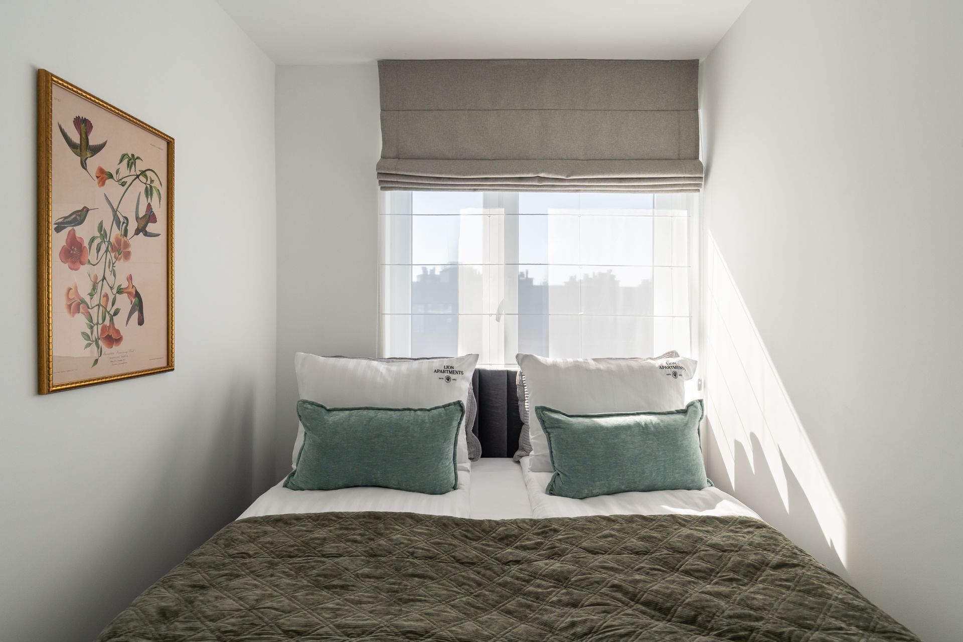 Une chambre à coucher avec un lit, des oreillers, une couverture matelassée, une fenêtre donnant sur un paysage agréable et une illustration botanique encadrée accrochée au mur.