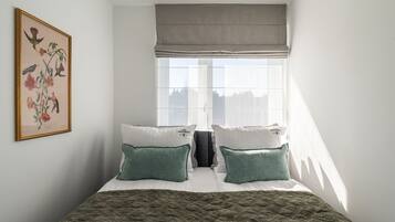 Une chambre à coucher avec un lit, des oreillers, une couverture matelassée, une fenêtre donnant sur un paysage agréable et une illustration botanique encadrée accrochée au mur.