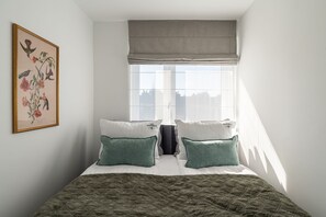A bedroom with a bed, pillows, a quilted blanket, a window with a view, and a framed botanical illustration on the wall. - Secret Garden by Lion Apartments Gdańsk (Gdańsk)