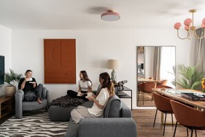 A modern living room with a sofa, a coffee table, and a dining area with chairs. - Secret Garden by Lion Apartments Gdańsk (Gdańsk)