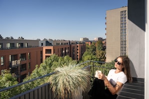 A person sitting on a balcony with a view of a cityscape, including buildings and a clear sky. - Secret Garden by Lion Apartments Gdańsk (Gdańsk)