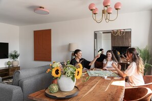 Un grupo de personas jugando un juego de mesa en una mesa de madera en una sala de estar moderna con un sofá gris, un espejo grande y una araña.