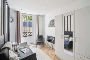 A modern living room with a sofa, a chair, a TV, and a wardrobe. - Chic Central Paris 1-Bedroom - Walk to Les Halles (Paris)