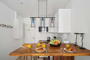 Une cuisine moderne avec des meubles blancs, une table à manger en bois dressée pour le petit-déjeuner et des luminaires suspendus au-dessus.