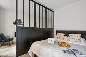 A modern bedroom with a bed, a side table, a chair, and a wardrobe. - Chic Central Paris 1-Bedroom - Walk to Les Halles (Paris)
