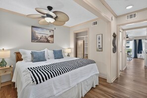 Una camera da letto con un letto, lampade sui comodini, una ventola a soffitto, un quadro e un corridoio che porta a un balcone.