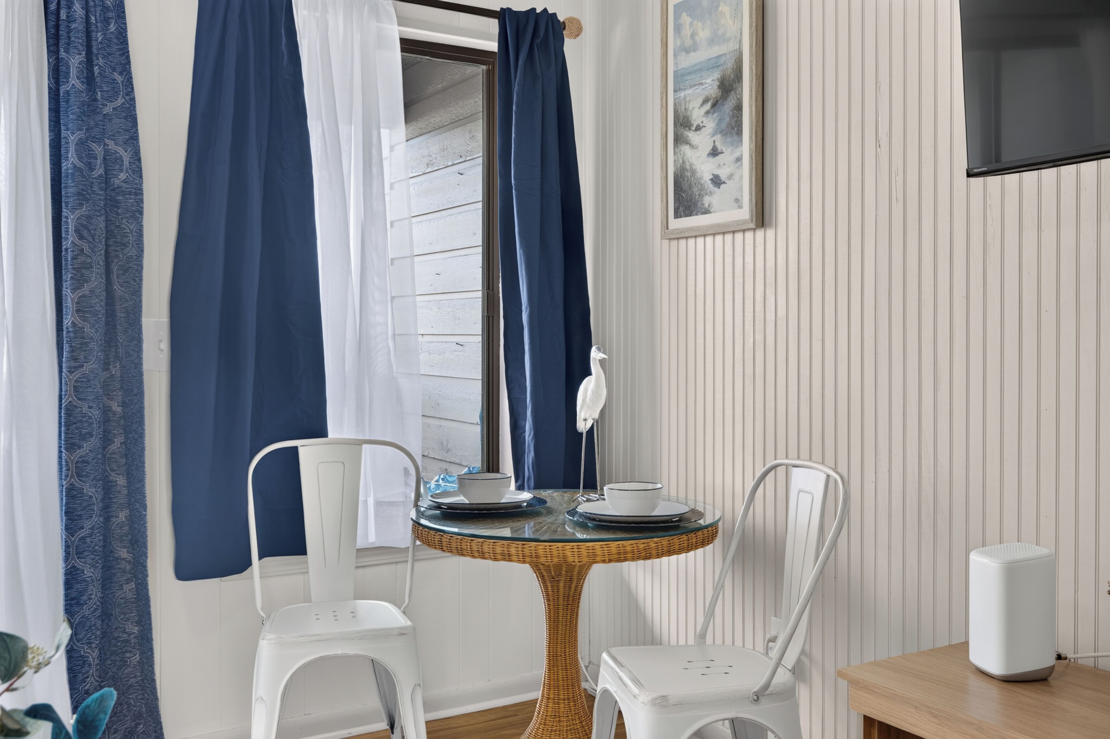 Un coin repas avec une table ronde, deux chaises, un oiseau blanc perché sur un support et un tableau accroché au mur.