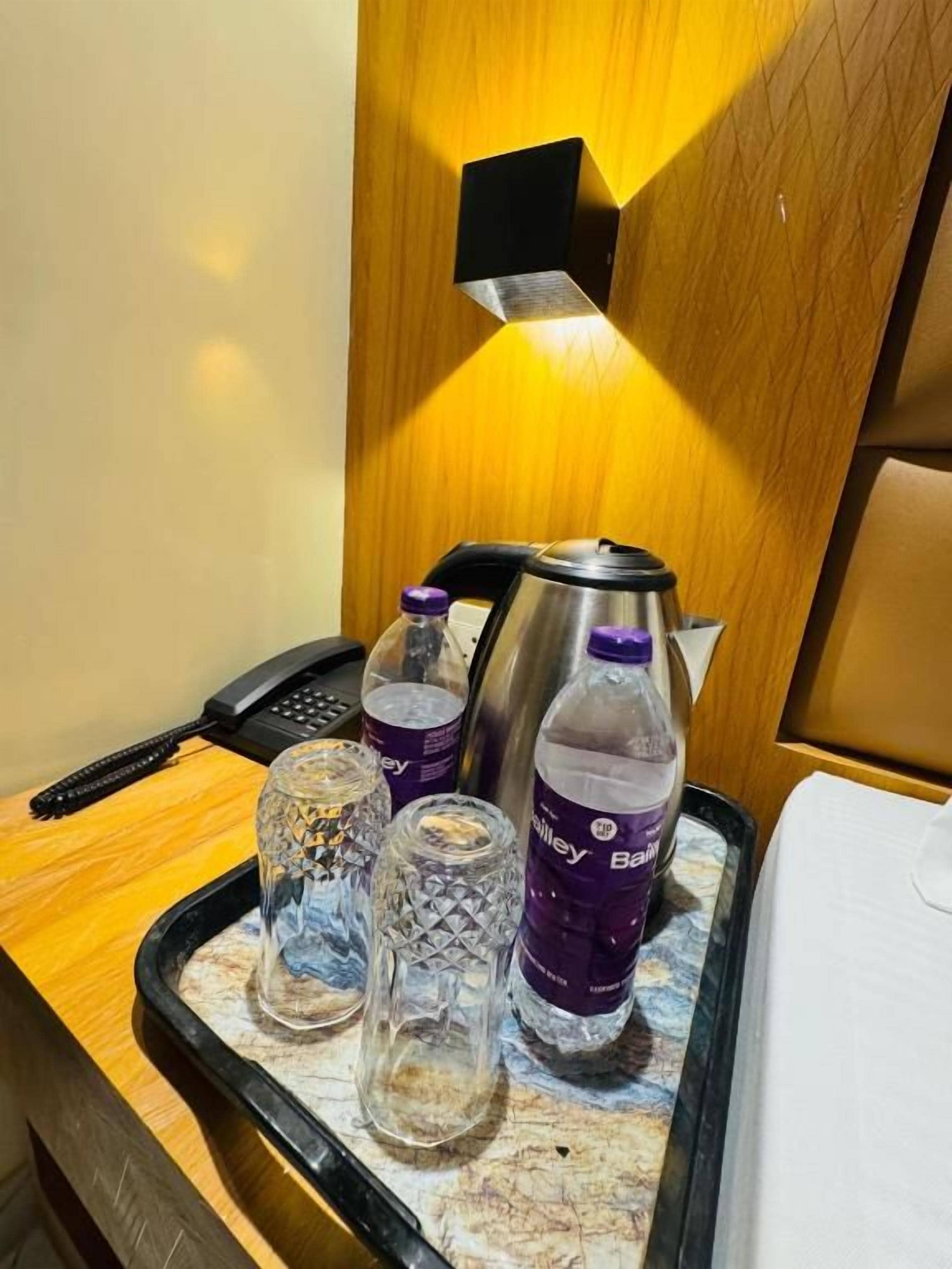Angolo del minibar in una camera d'albergo, con una bottiglia d'acqua, un bicchiere e una macchina per caffè.